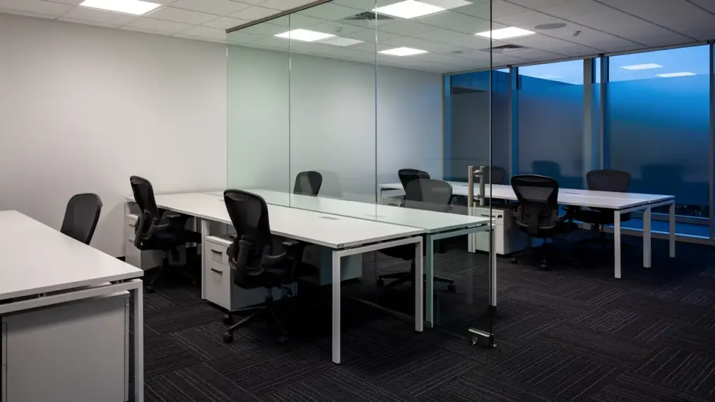 A small office after hours with wiped desks, a clean glass partition and freshly vacuumed carpet tiles